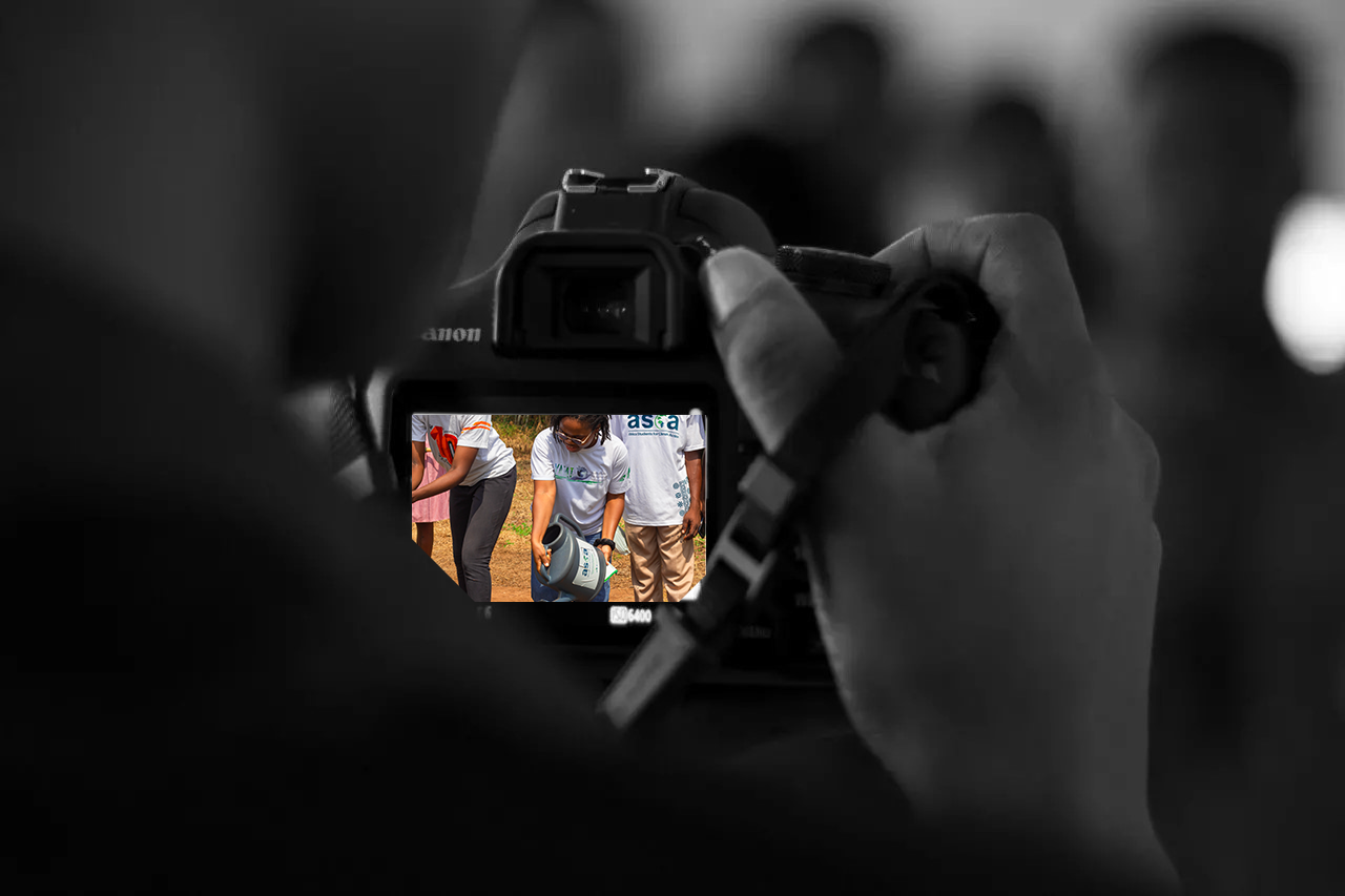 A camera operator frames a community tree-planting activity on the camera screen.